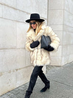 Woman walking outdoors in a cream-colored faux fur coat and black accessories.