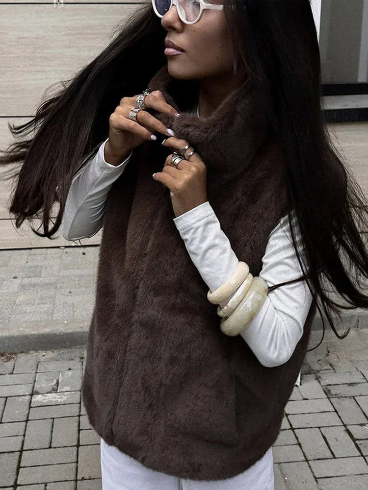 Woman adjusting the high collar of her brown faux fur vest, showing off accessories.