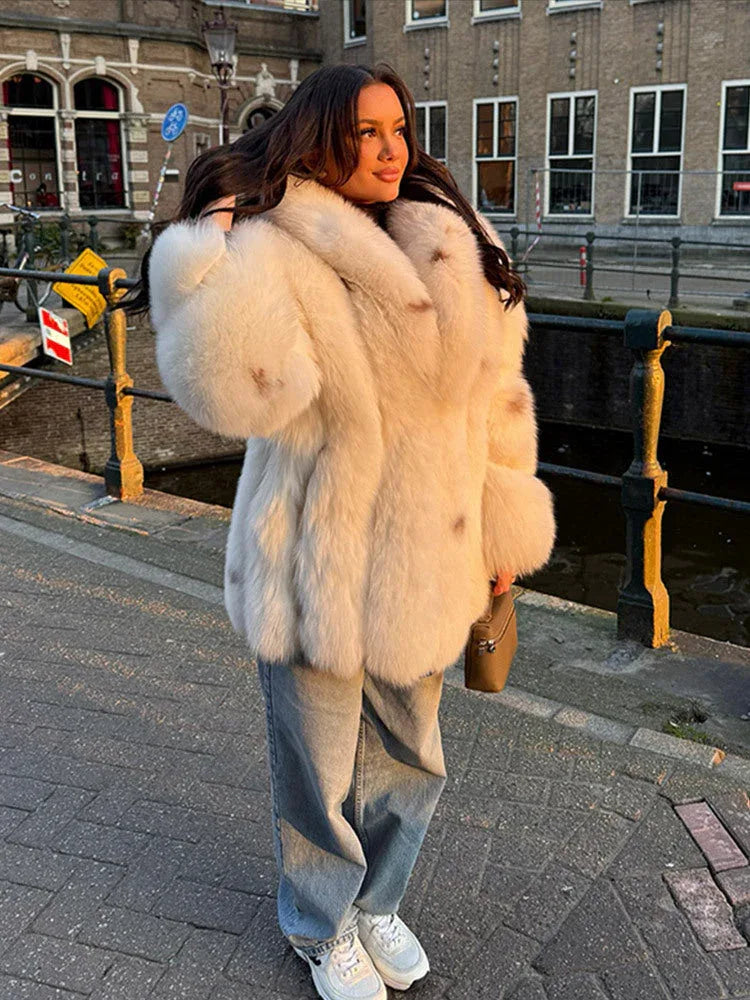 Woman in a cream-colored faux fur coat with a prominent collar, outdoors.