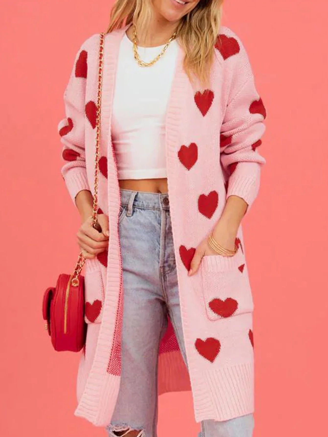 Front view of a woman in a pink heart print cardigan, white top, and blue jeans.