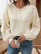 Woman holding a mug while wearing a cream knit sweater with floral details.