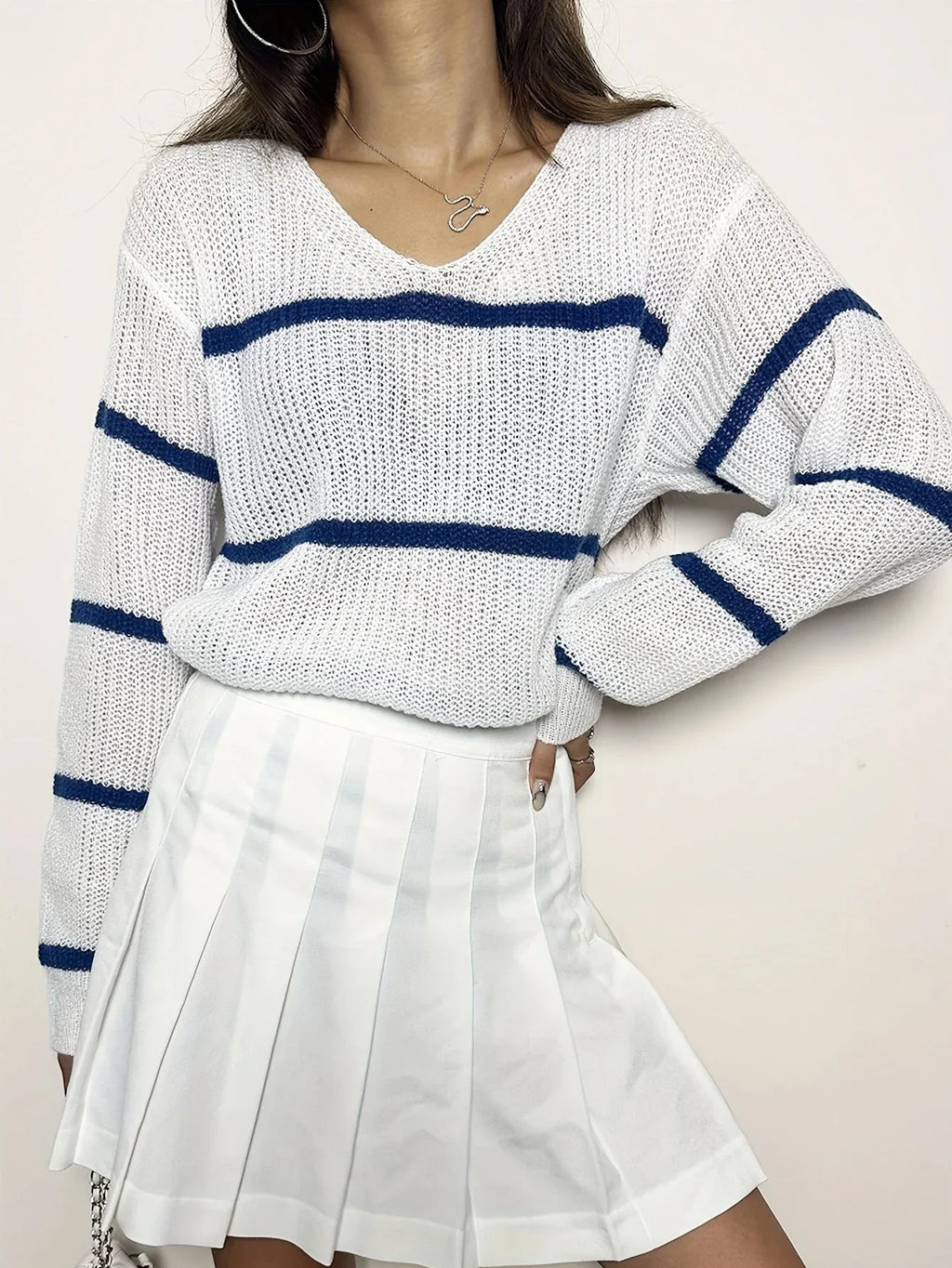 Front view of a woman in a white and navy blue striped knit sweater, posing with her hand on her hip.