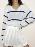 Front view of a woman in a white and navy blue striped knit sweater, posing with her hand on her hip.