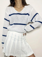 Front view of a woman in a white and navy blue striped knit sweater, posing with her hand on her hip.