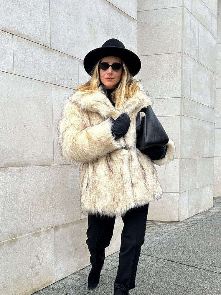 Woman walking in a cream-colored faux fur coat, black pants, black boots, and black hat.