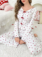 Close-up of a woman wearing a white long-sleeve pajama top with a red heart print and red trim, featuring decorative bows at the neckline.