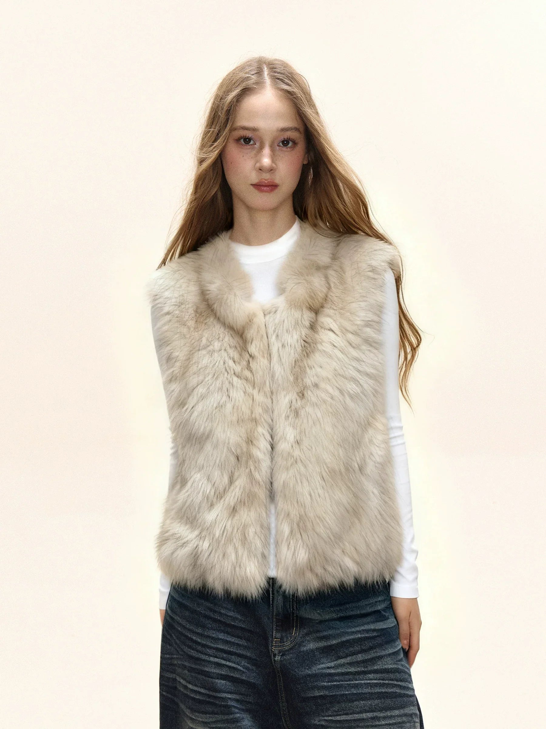 Woman wearing a cream faux fur vest over a white long-sleeve shirt and denim skirt.