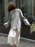 Woman in a light grey oversized sweater and white skirt holding flowers
