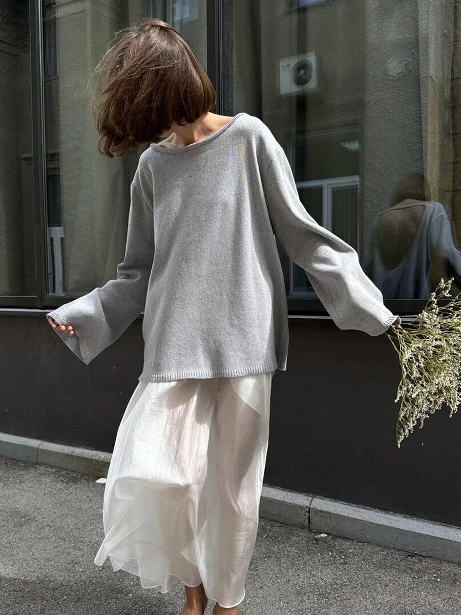 Woman in a light grey oversized sweater and white skirt holding flowers