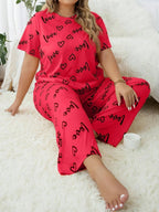 Woman wearing a red short-sleeve pajama top and pants with a black heart and 'love' graphic print, sitting on the floor.