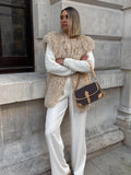 Woman wearing a tan faux fur vest over a white cable-knit sweater and white wide-leg pants.