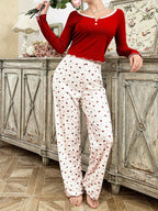 Woman wearing red long-sleeve top and white patterned pajama pants, holding flowers.