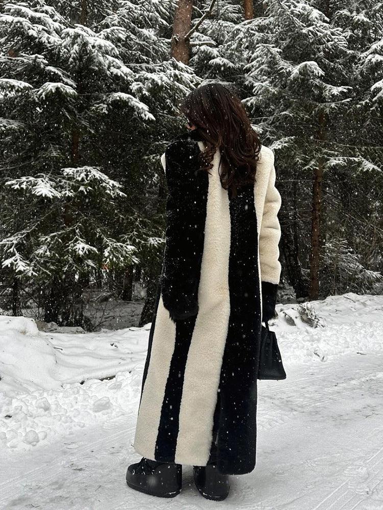 Woman seen from behind in a black and white vertical striped long faux fur coat, standing in a winter landscape.