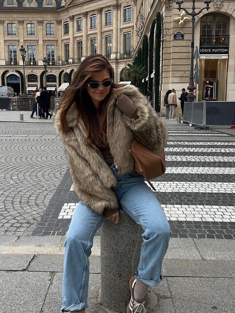Woman wearing a brown faux fur jacket with a collared neckline and zipper closure, sitting on a stone pillar.
