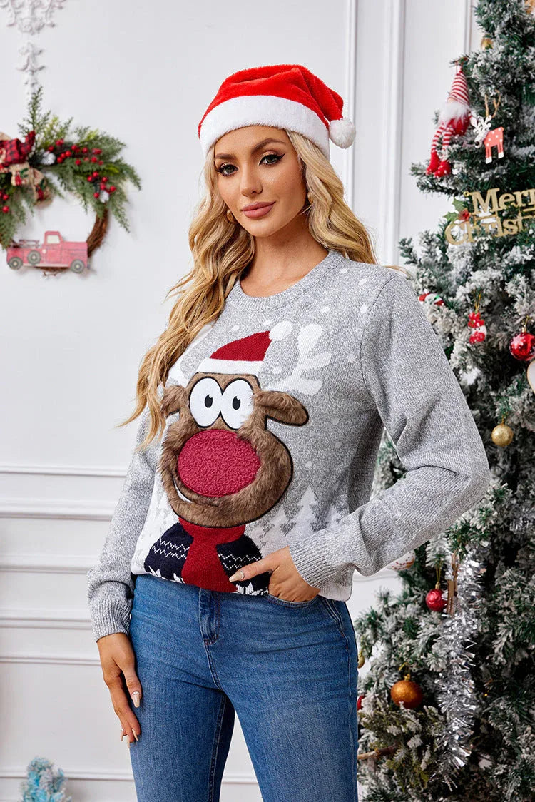 Woman wearing a grey long-sleeve knit sweater with a large reindeer graphic and snowflake pattern, paired with blue jeans and a red Santa hat.