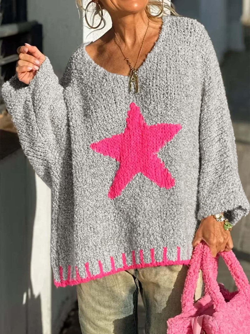 Woman holding a pink fuzzy bag while wearing a gray knit sweater with a pink star graphic.