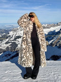 Woman wearing a long leopard print faux fur coat standing on a snowy mountain.