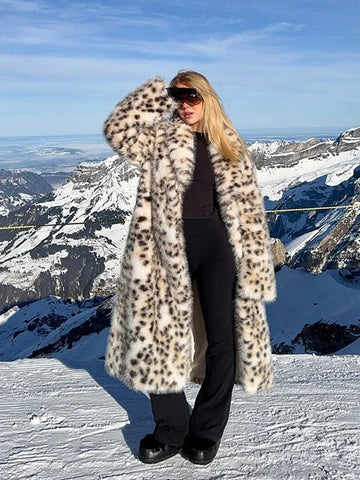 Woman wearing a long leopard print faux fur coat standing on a snowy mountain.