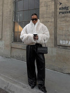 Woman wearing a white faux fur jacket and wide-leg black pants, holding a coffee cup.