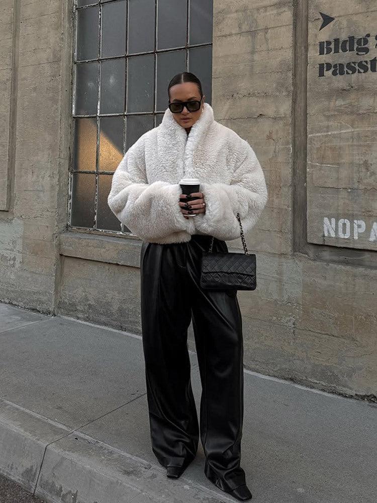 Woman wearing a white faux fur jacket and wide-leg black pants, holding a coffee cup.