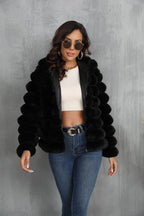 Woman in a black hooded faux fur jacket, showcasing the zipper closure and cropped style.