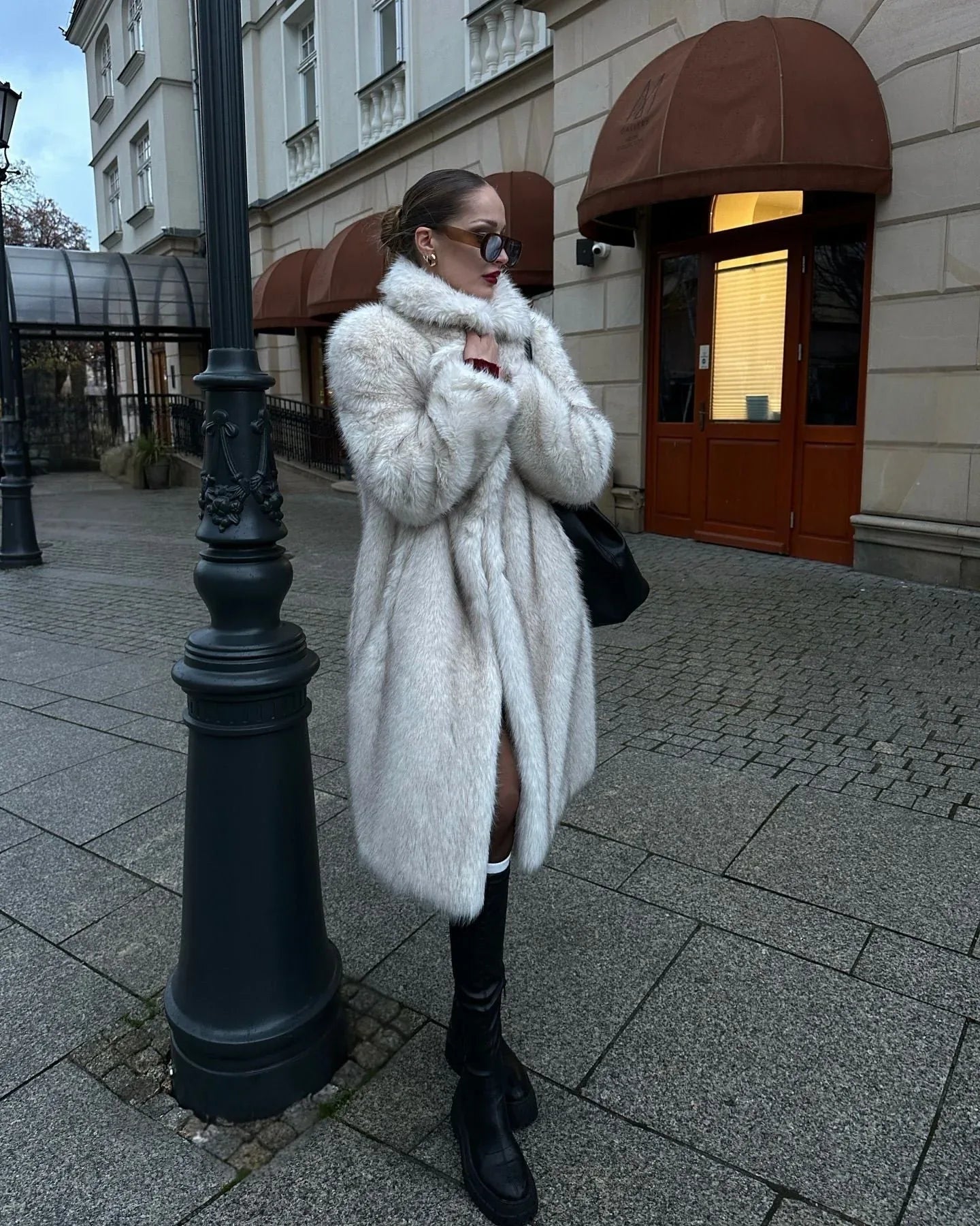 Side view of a woman in a white faux fur coat, a dark top, and black boots.