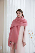 Woman wearing a pink oversized scarf draped over a light pink coat, standing indoors.