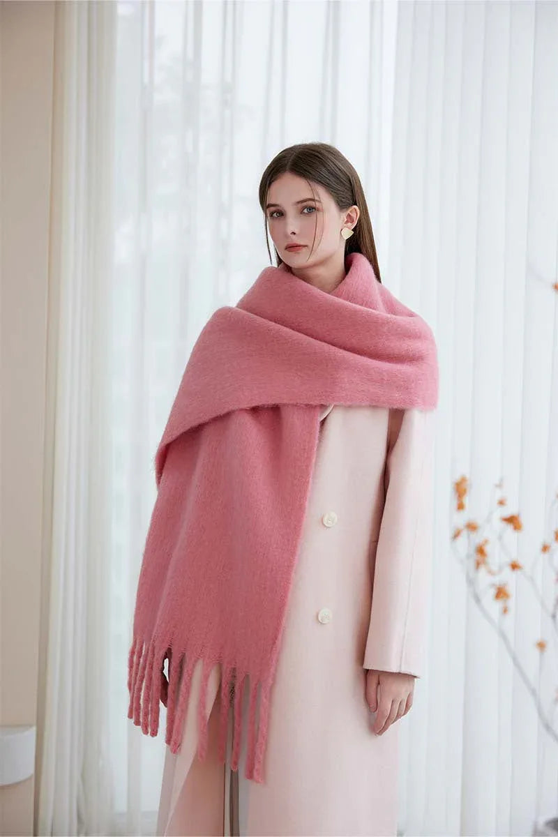 Woman wearing a pink oversized scarf draped over a light pink coat, standing indoors.