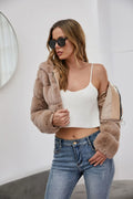 Woman wearing a taupe faux fur jacket, open to reveal a white crop top and blue jeans.
