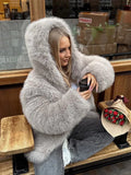 Woman in a grey hooded faux fur jacket holding a coffee cup