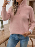 Woman holding a phone, wearing a pink hooded knit sweater and blue denim jeans