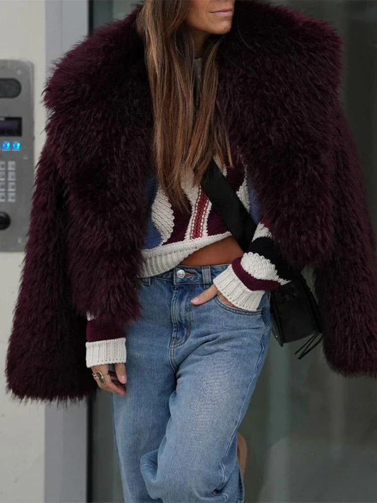 Woman wearing a burgundy faux fur cropped jacket with a wide lapel, paired with a striped sweater and blue jeans.