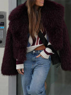 Woman wearing a burgundy faux fur cropped jacket with a wide lapel, paired with a striped sweater and blue jeans.