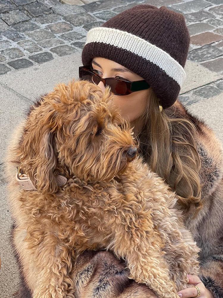 Close-up of a woman in a faux fur coat and knit hat, holding a small dog.