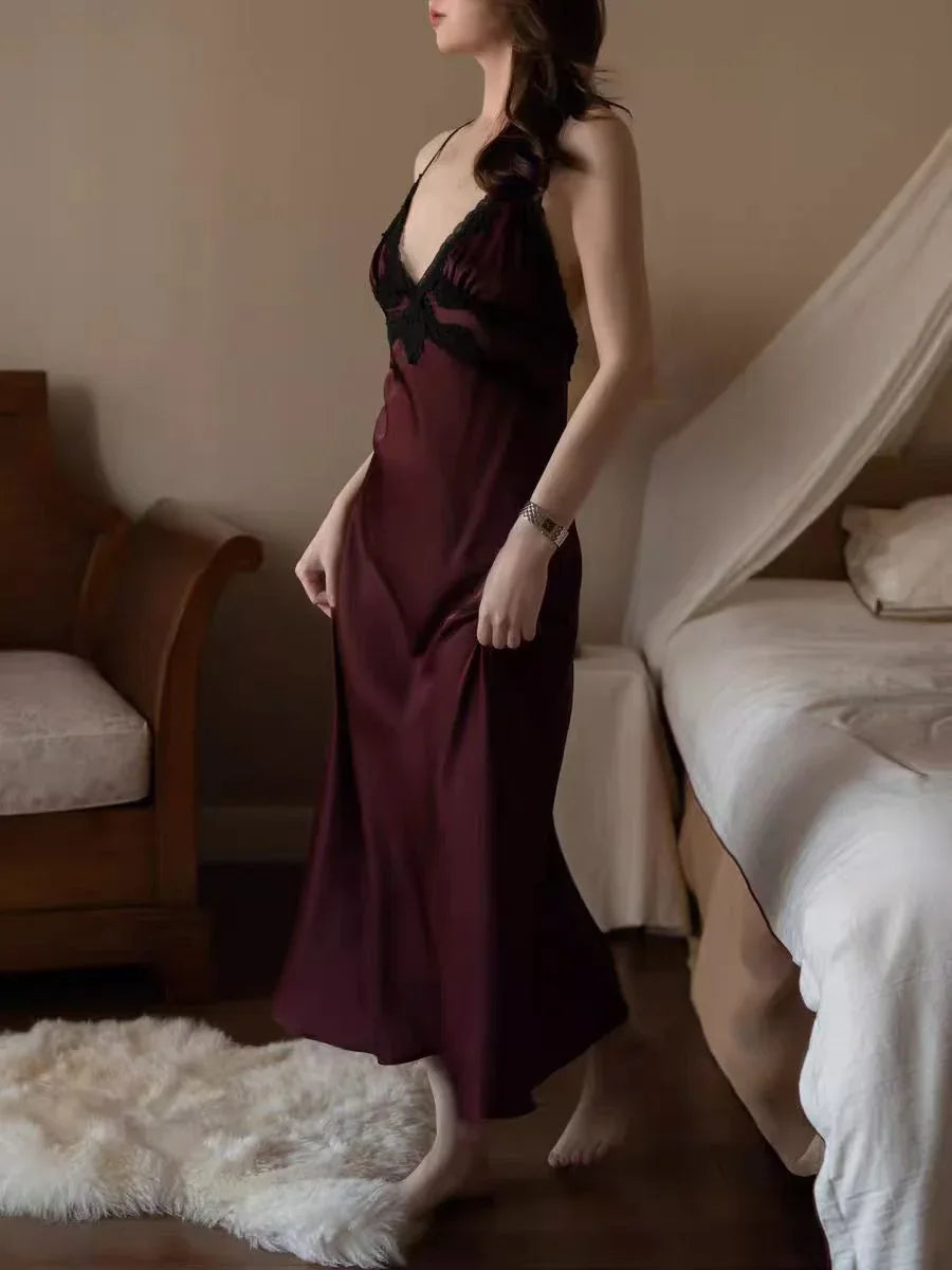 Woman in a burgundy satin slip dress walking in a bedroom.