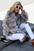 Woman sitting on the ground wearing a grey faux fur jacket and white ripped jeans