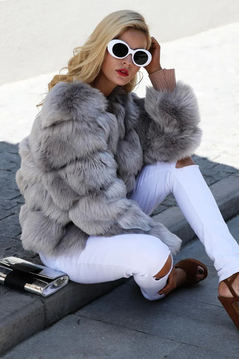 Woman sitting on the ground wearing a grey faux fur jacket and white ripped jeans