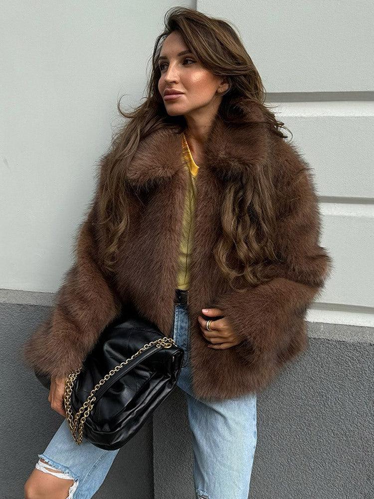 Woman wearing a brown faux fur jacket with long sleeves and an oversized collar, holding a white cup.