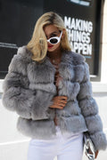 Woman wearing a grey faux fur cropped jacket with white pants and sunglasses