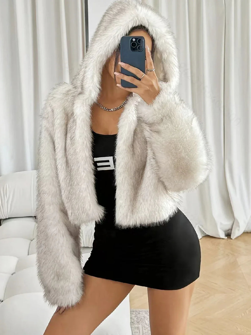Woman taking a mirror selfie in a white faux fur cropped hooded jacket