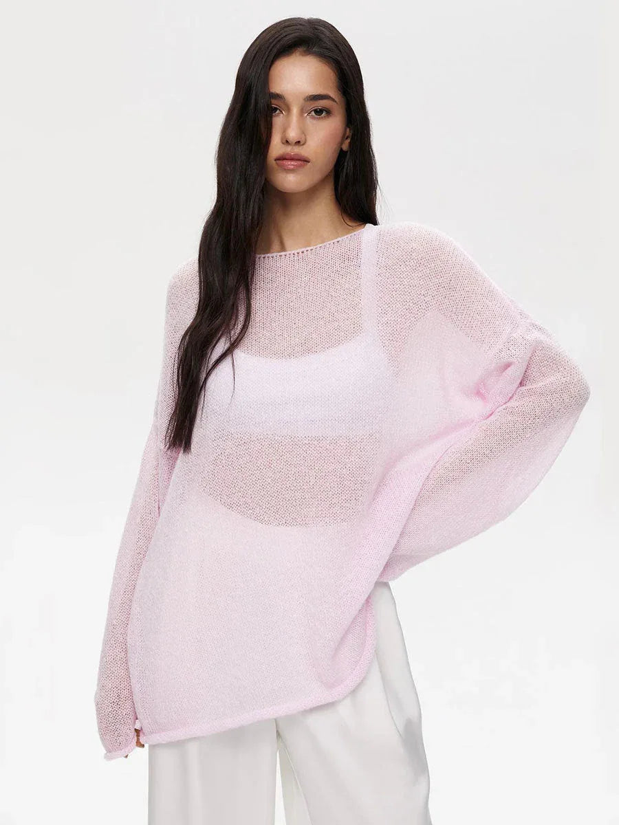 Woman wearing a pink oversized sheer knit sweater and white pants.