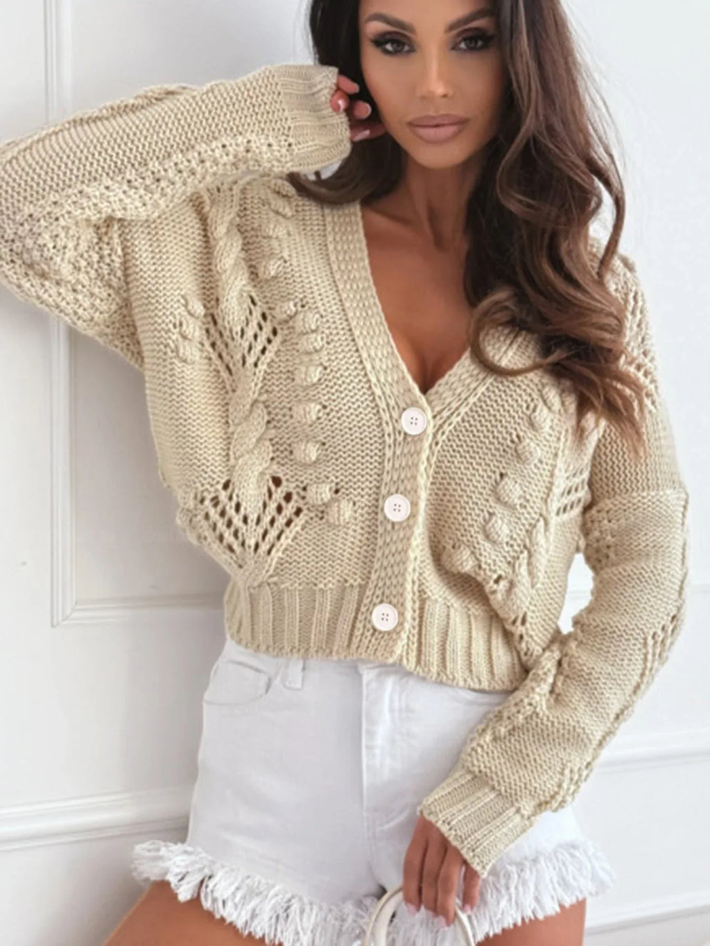 Close-up of a beige cropped knit cardigan with intricate open knit and cable knit details.
