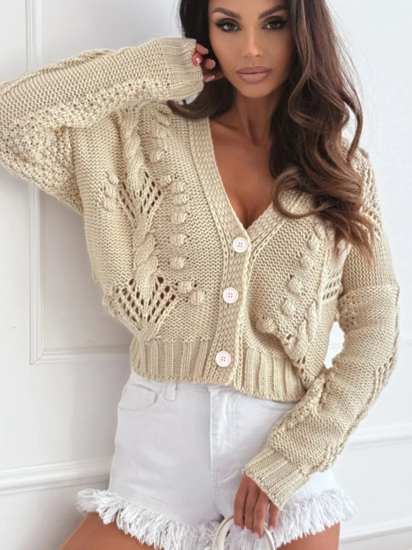 Close-up of a beige cropped knit cardigan with intricate open knit and cable knit details.