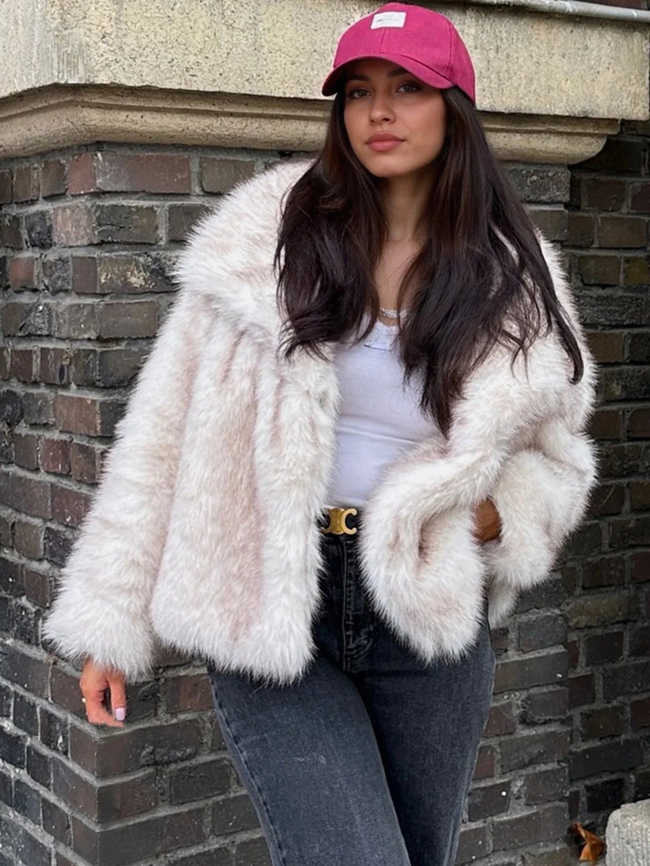Full body shot of a woman in a cream faux fur jacket and dark jeans, standing outdoors.