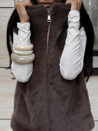 Front view of a woman wearing a brown faux fur vest with a zipper closure, layered over a white long-sleeved shirt.