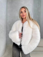 Woman wearing a white faux fur cropped jacket with an open front and long sleeves.