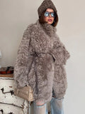 Woman demonstrating the belted feature of a grey curly faux fur coat, tied at the waist with a dark leather belt.