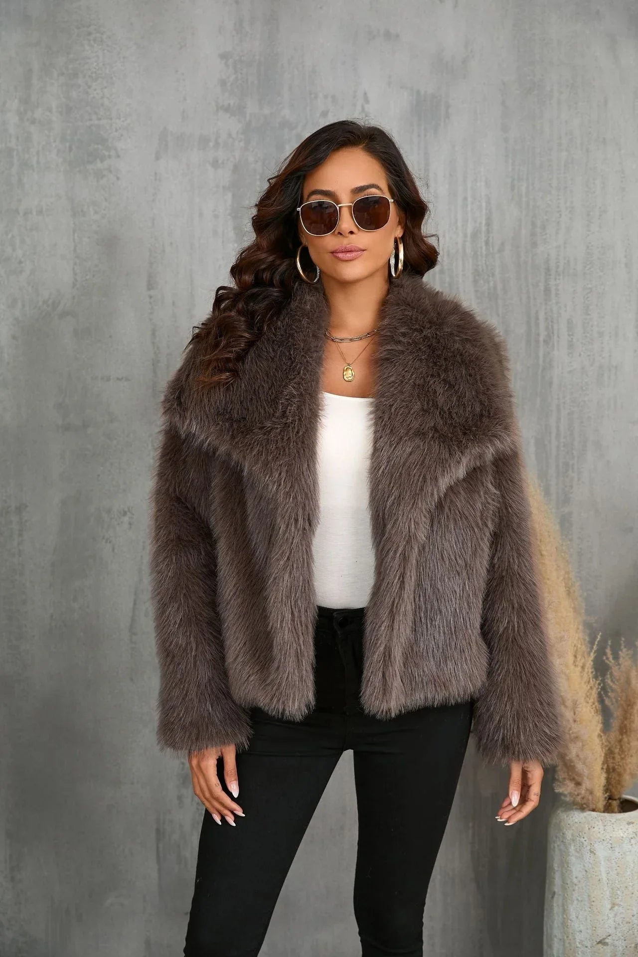 Woman posing in a brown faux fur cropped jacket, sunglasses and gold jewelry