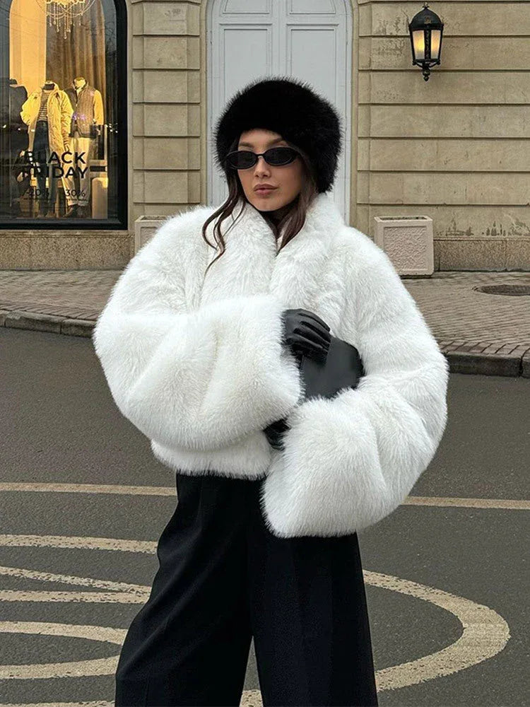 Woman wearing a white fluffy faux fur cropped jacket with black pants and a black hat.