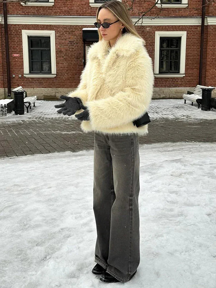 Woman wearing a cream faux fur jacket with wide lapels, grey wide-leg jeans, and black gloves, standing in the snow. Main image